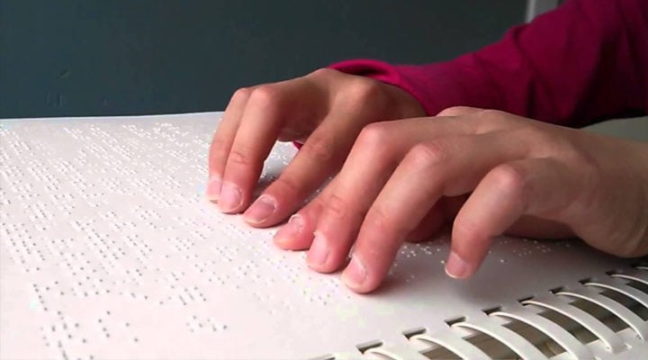 Hands reading a page of Braille text