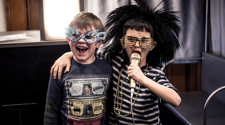 Two boys with rock star glasses, gold microphone and 80s rock wig.
