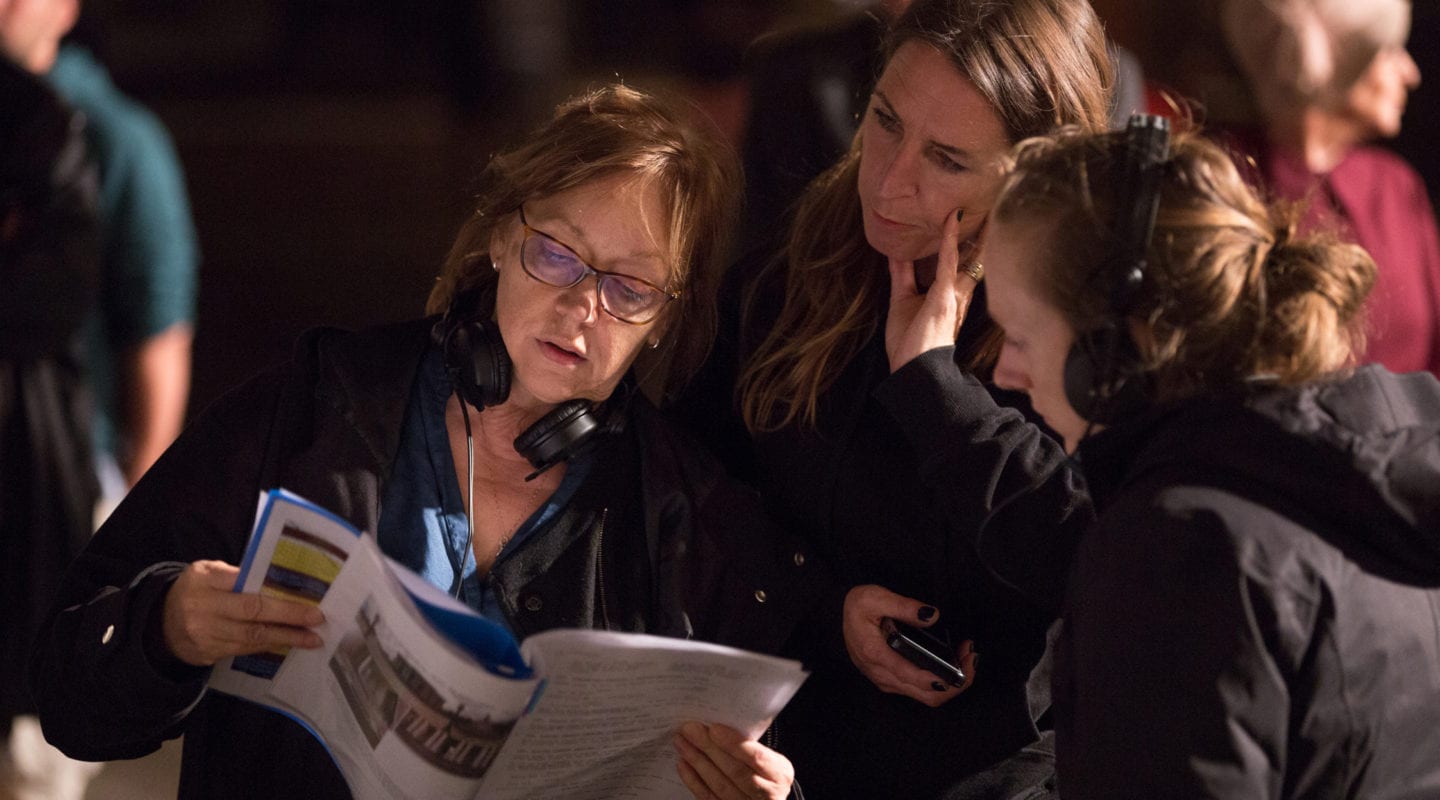 Three women wearing headsets looking at a script