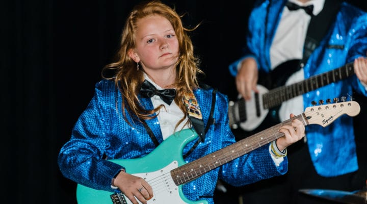 Girl playing electric guitar in a sequined tuxedo
