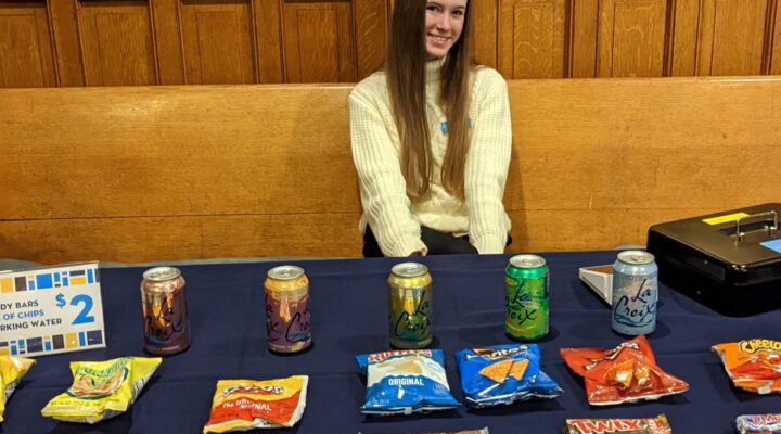 Smiling DPO volunteer in front of table with snacks and sparkling waters displayed on top of it